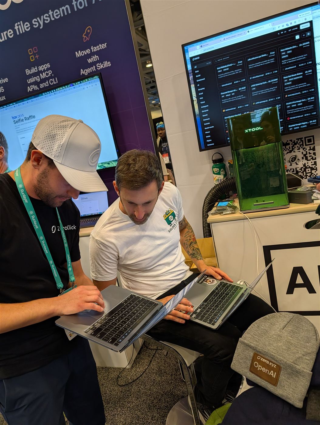 Two people setting up a design on laptops next to the laser at a conference booth