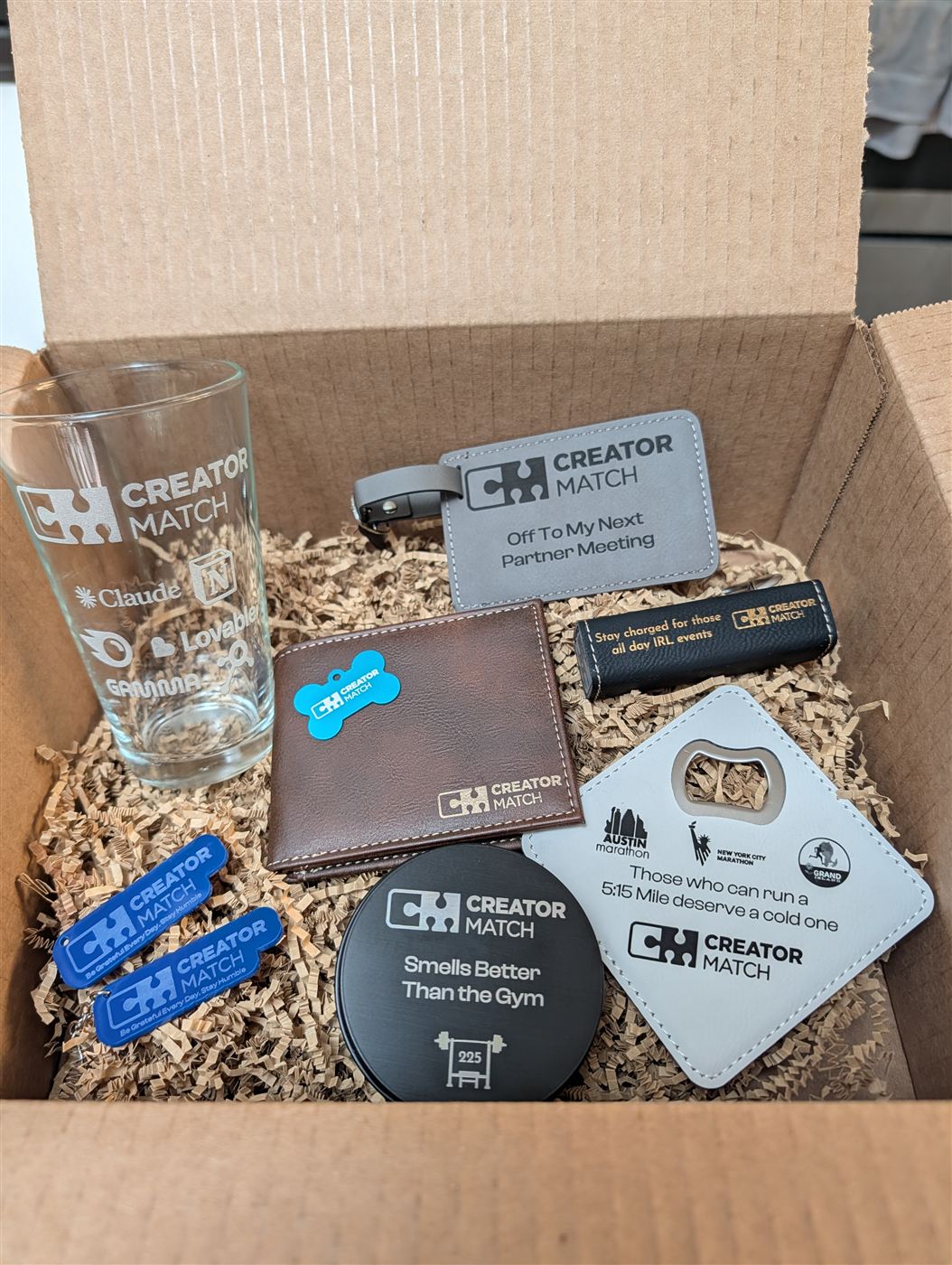 Gift box of engraved items including a pint glass, wallet, luggage tag, candle tin, and coaster bottle opener